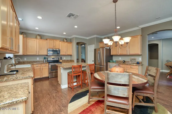 a kitchen with stainless steel appliances granite countertop a stove top oven a sink a dining table and chairs with wooden floor