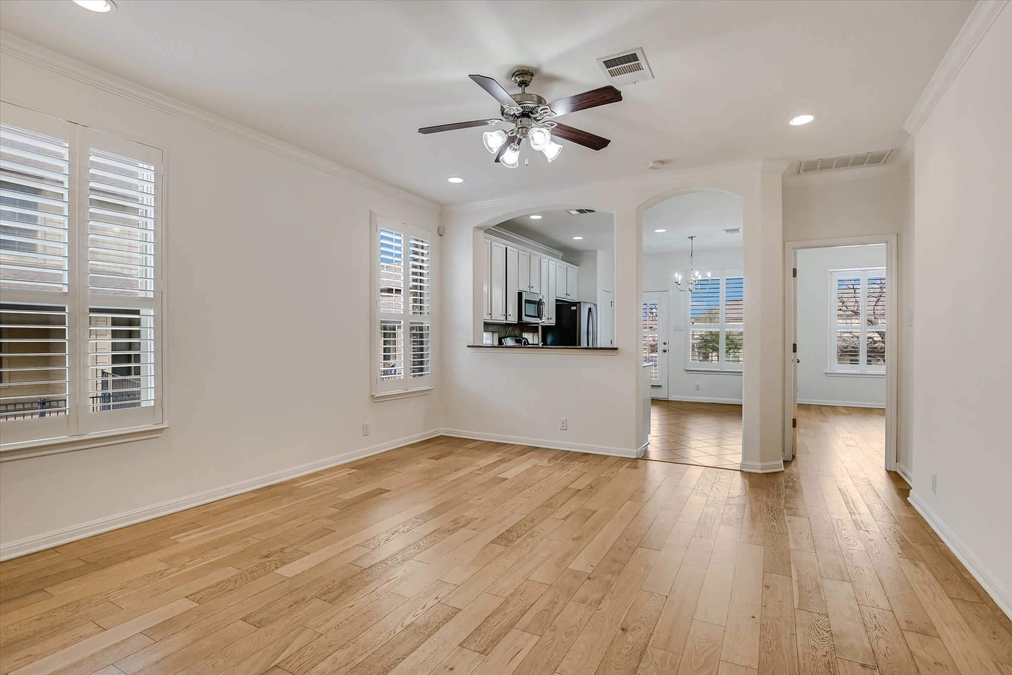 14001 Avery Ranch Boulevard, Unit 1601 Austin, TX 78717 - Photo 4 of 25 Unfurnished living room featuring a ceiling fan, light wood-style floors, crown molding, a chandelier, kitchen bar and arched walkways