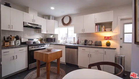 a kitchen with stainless steel appliances a sink a stove a refrigerator cabinets and dining table