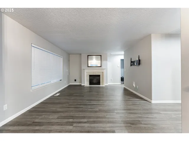 a view of an empty room with wooden floor and fireplace