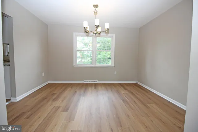 an empty room with wooden floor chandelier and window