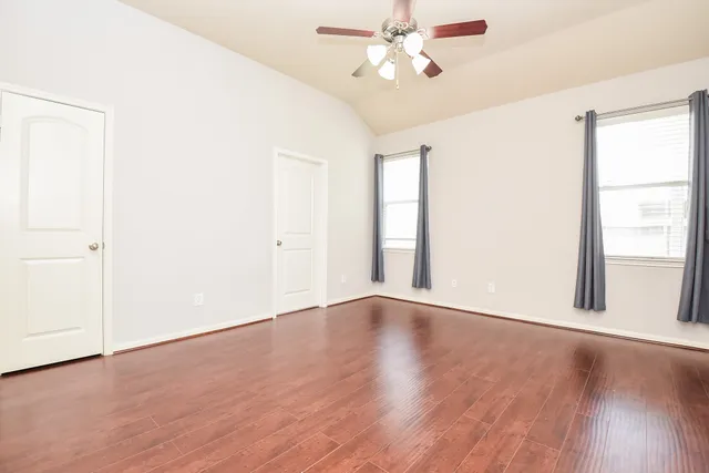 an empty room with wooden floor fan and windows
