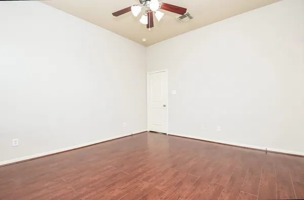 an empty room with wooden floor and fan