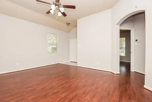 an empty room with wooden floor chandelier fan and windows