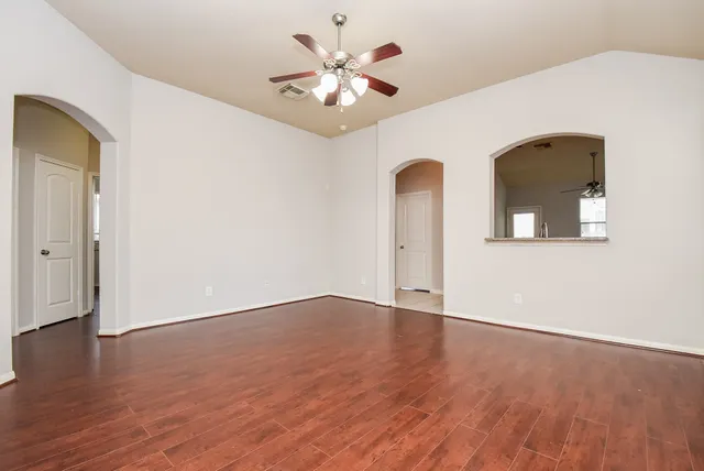 a view of an empty room with wooden floor and a ceiling fan