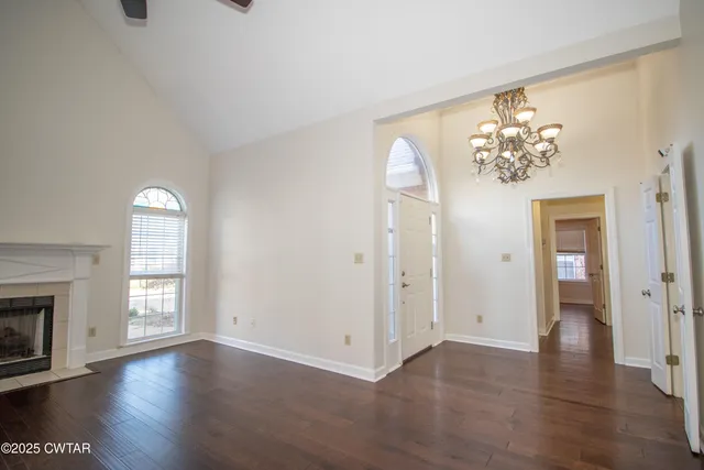 an empty room with wooden floor chandelier and windows