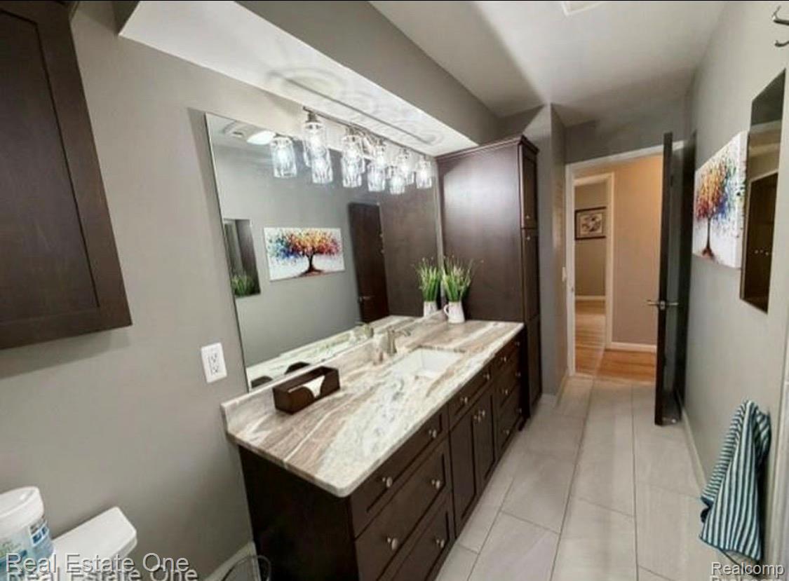 1115 Torpey Road Troy, MI 48083 - Photo 27 of 38 Double vanity featuring a light-toned stone countertop, dual undermount sinks, dark wood cabinetry, and a multi-bulb light fixture