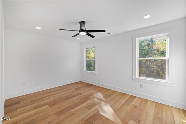 a view of empty room with wooden floor and fan