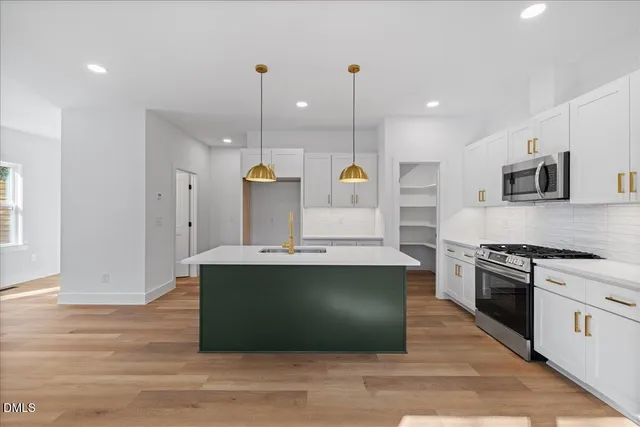 a view of kitchen with kitchen island stainless steel appliances a stove a sink and a wooden floor