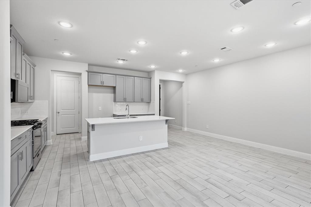 519 Sequoia Street Allen, TX 75002 - Photo 13 of 38 Open-concept kitchen featuring an island with an undermount sink, gray cabinetry, white countertops, and stainless steel appliances