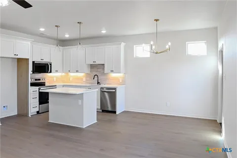 a kitchen with kitchen island granite countertop a stove a sink a refrigerator and white cabinets with wooden floor