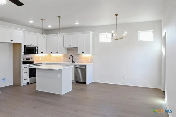 a kitchen with kitchen island granite countertop a stove a sink a refrigerator and white cabinets with wooden floor