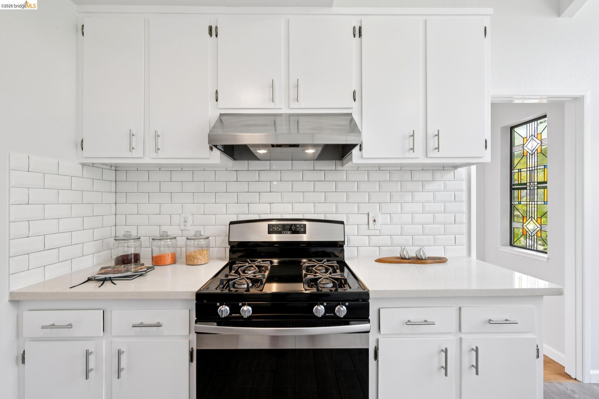 1340 Henry Street Berkeley, CA 94709 - Photo 20 of 52 Kitchen featuring a stainless steel range, white subway tile backsplash, white cabinetry with silver hardware, light-toned countertops, and a decorative stained glass window