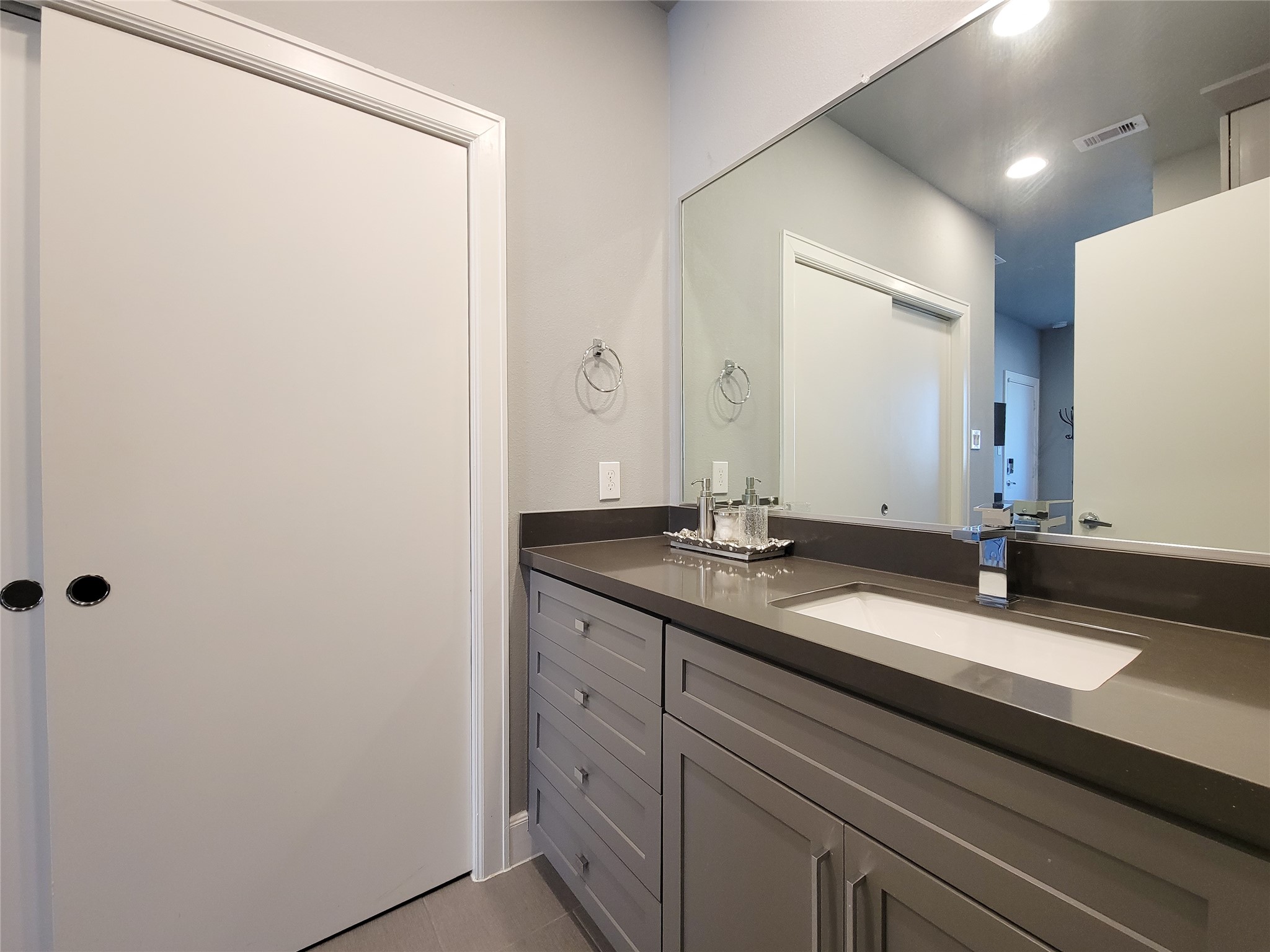 1705 Eado Point Lane Houston, TX 77003 - Photo 11 of 50 1st Floor Bedroom offers a modern bathroom with a sleek, gray vanity featuring a large mirror and ample storage space. Neutral tones create a clean, sophisticated look. The closet offers conventient connects for a stackable washer/dryer and built-in shelves.