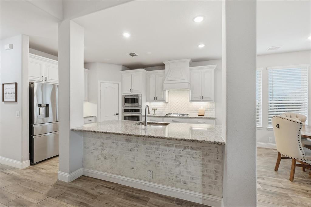 924 Timber Ridge Drive Justin, TX 76247 - Photo 10 of 32 Open-concept kitchen featuring white cabinetry, stainless steel appliances, a large island with a brick facade, and wood-finish flooring
