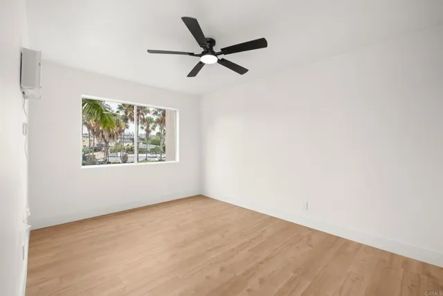 a view of an empty room with wooden floor and a ceiling fan