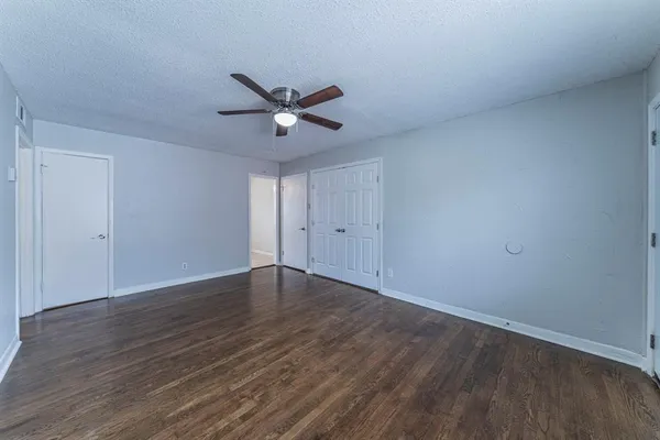 a view of an empty room with wooden floor and a ceiling fan
