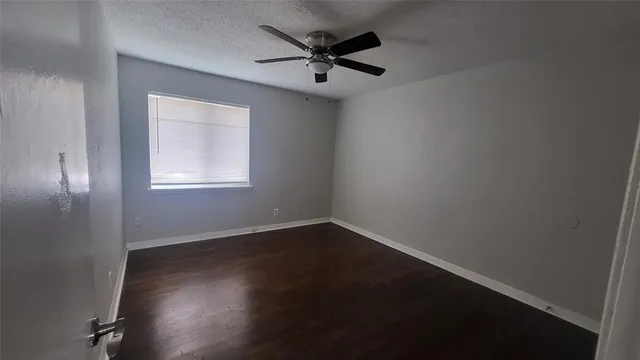 an empty room with wooden floor fan and windows
