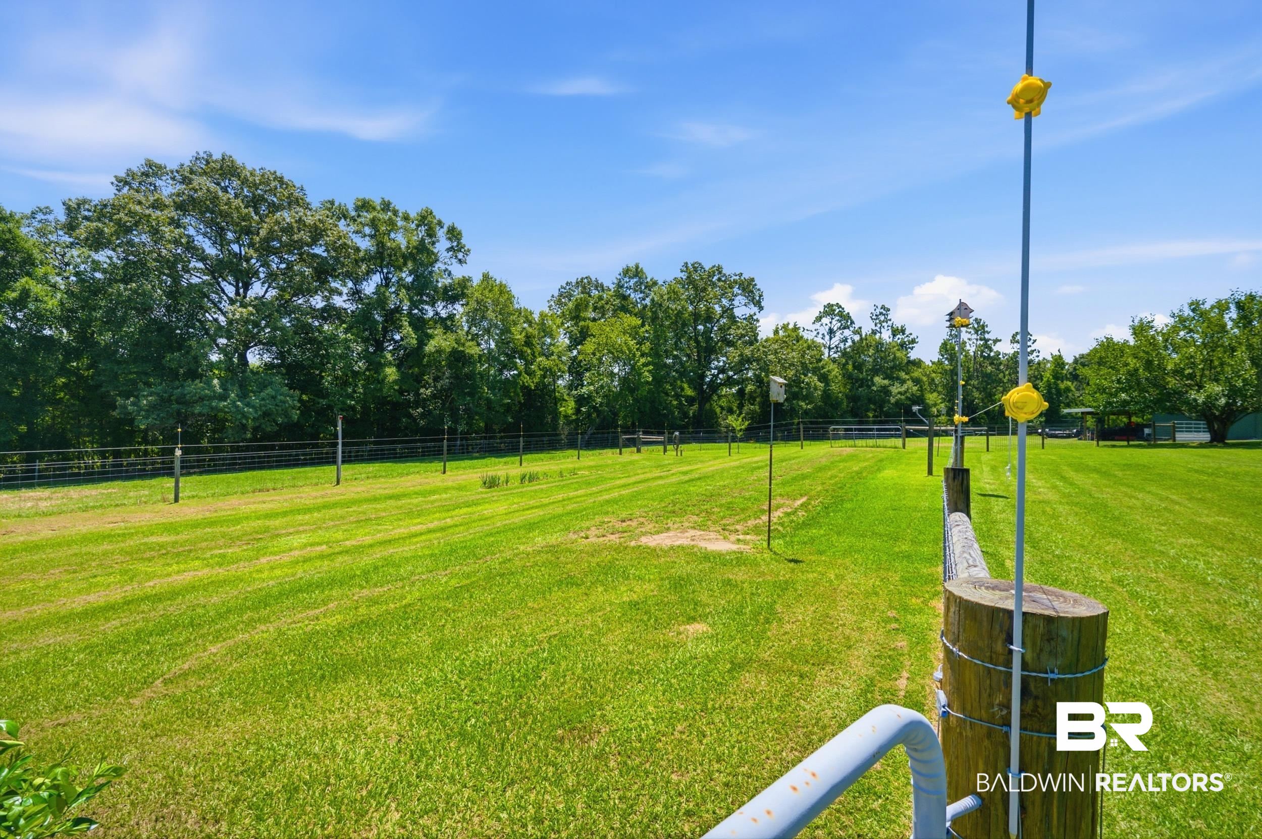 15855 Calvin Richerson Road Bay Minette, AL 36507 - Photo 66 of 83 Expansive green lawn with a perimeter fence, mature trees providing natural screening, and a wooden post with an attached gate mechanism