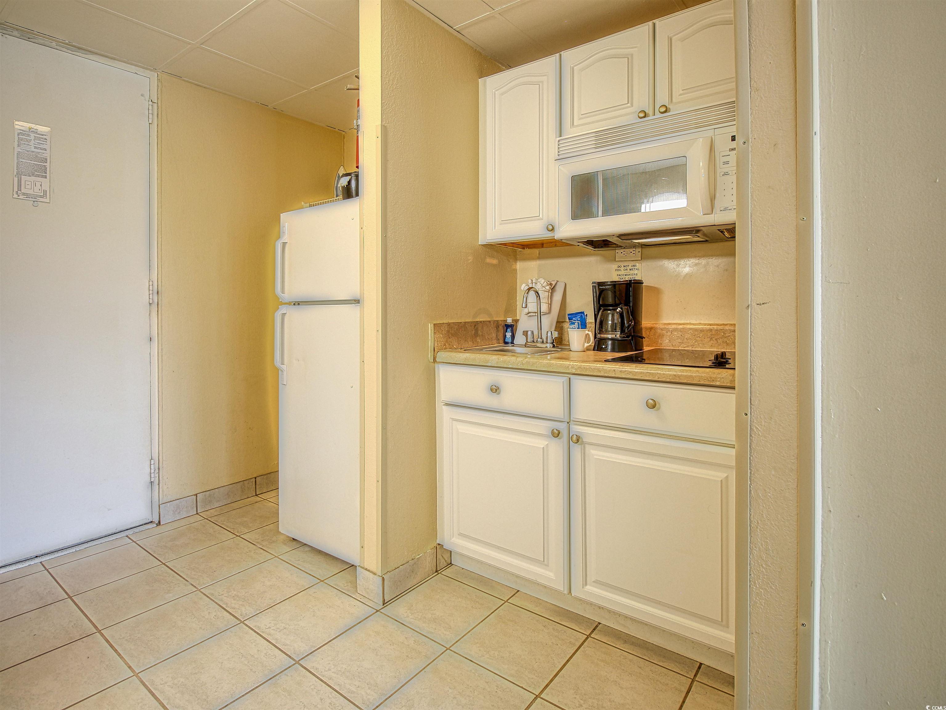 6803 North Ocean Boulevard, Unit 314 Myrtle Beach, SC 29572 - Photo 10 of 19 Kitchen with white appliances, white cabinets, a paneled ceiling, and light tile patterned floors