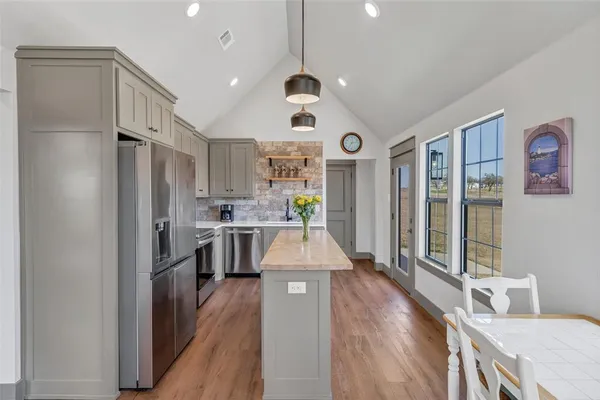 a kitchen with stainless steel appliances granite countertop a refrigerator a oven a stove and a dining table with wooden floor