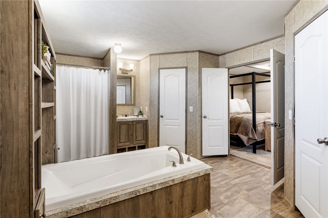 995 Diserens Road North Zulch, TX 77872 - Photo 31 of 41 Bathroom featuring a built-in soaking tub with a stone-finish surround, wood-finish cabinet his and her vanities with a vessel sinks, and an enclosed shower area