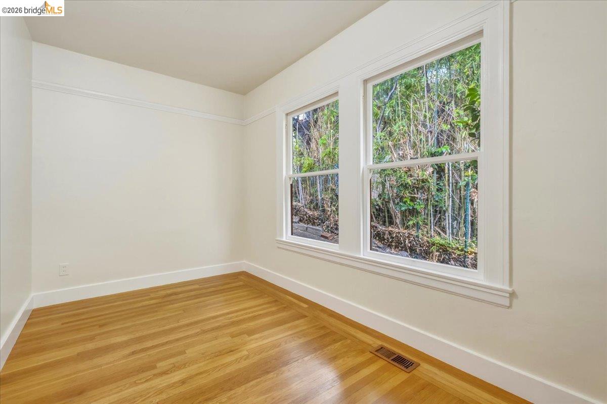 2403 Cedar Street Berkeley, CA 94708 - Photo 29 of 33 Room featuring two large windows with white trim, wood-finish flooring, a baseboard heating vent, and crown molding
