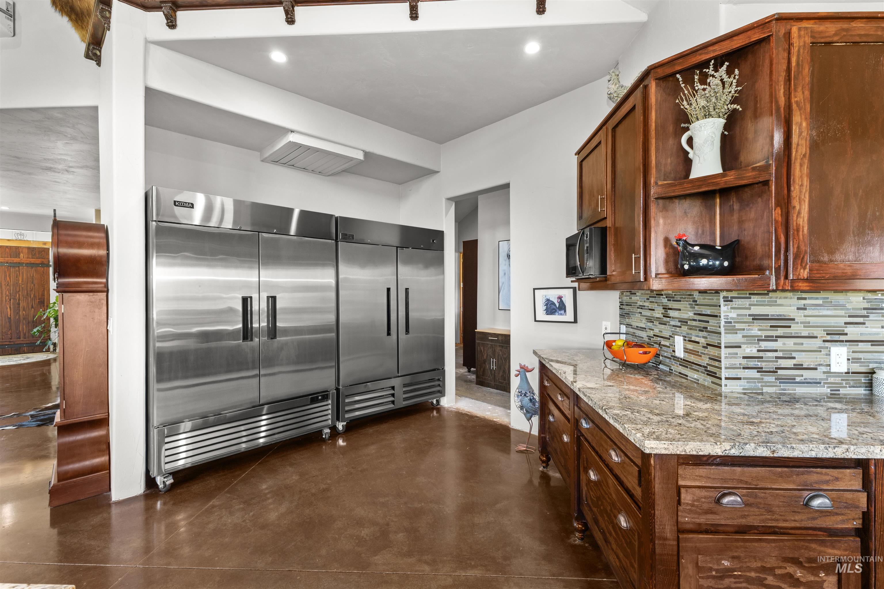 1030 Desert Glen Road Adrian, OR 97901 - Photo 24 of 47 Kitchen featuring multiple stainless steel commercial-grade refrigerators, rich wood cabinetry, a granite countertop, and a mosaic tile backsplash