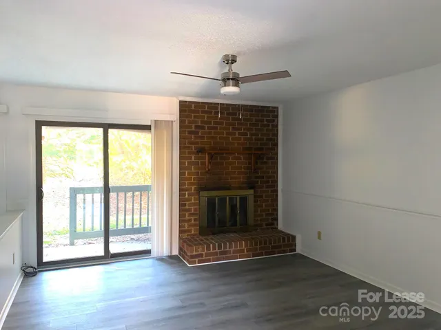 a view of an empty room with wooden floor fireplace and a window