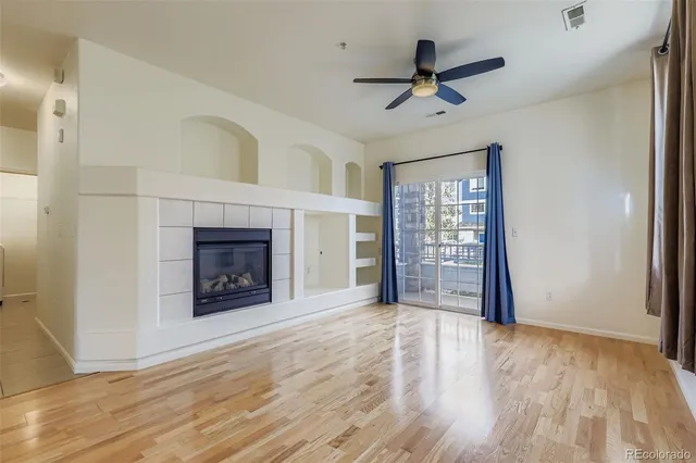 a view of an empty room with wooden floor fireplace and a window