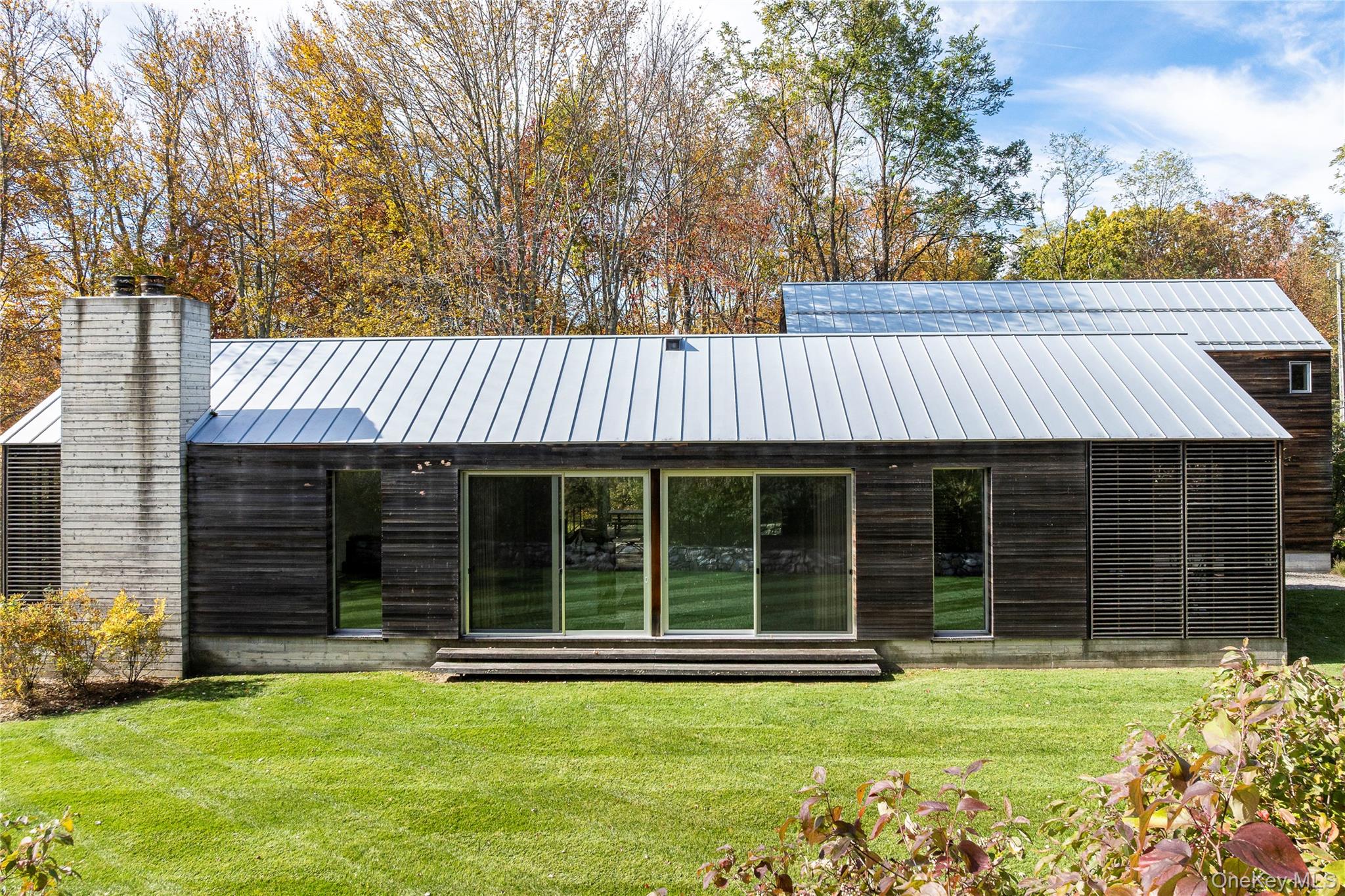 a view of a house with a large window and a yard with plants and large trees