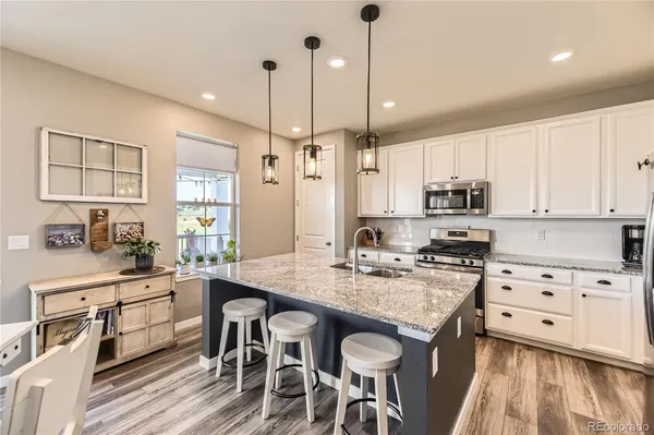 a kitchen with stainless steel appliances kitchen island granite countertop a stove a sink and white cabinets with wooden floor