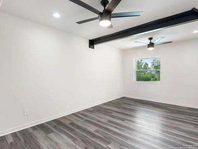 an empty room with wooden floor ceiling fan and windows