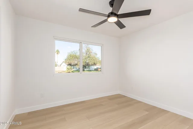 an empty room with wooden floor fan and windows
