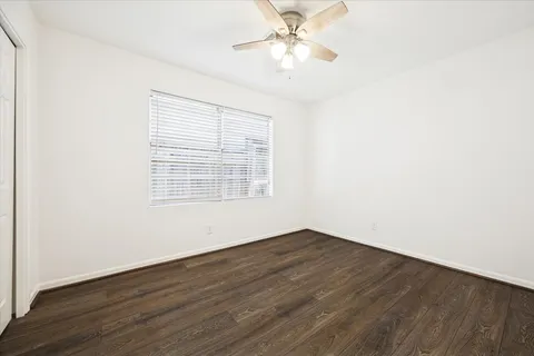 an empty room with wooden floor fan and windows