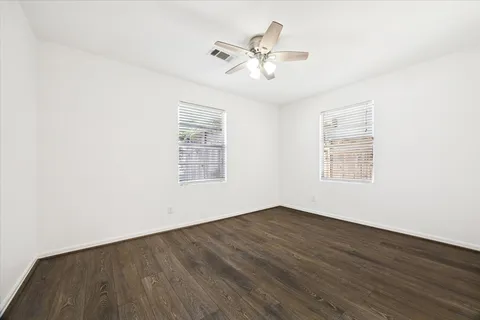 an empty room with wooden floor chandelier fan and windows