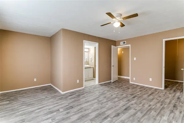 a view of an empty room with wooden floor and a ceiling fan