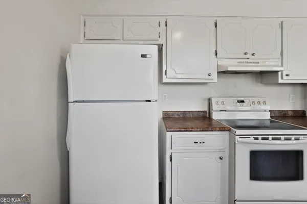 a white refrigerator freezer and a stove sitting inside of a kitchen with granite countertop white cabinets