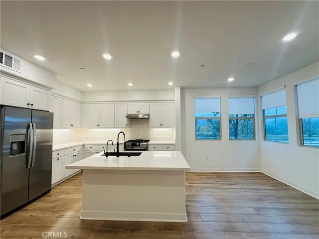 a view of kitchen with stainless steel appliances granite countertop a stove a sink a refrigerator and white cabinets with wooden floor