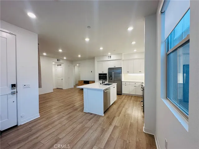 a view of a kitchen with kitchen island wooden floors stainless steel appliances and a window