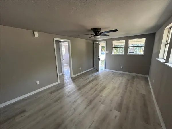 an empty room with wooden floor fan and windows