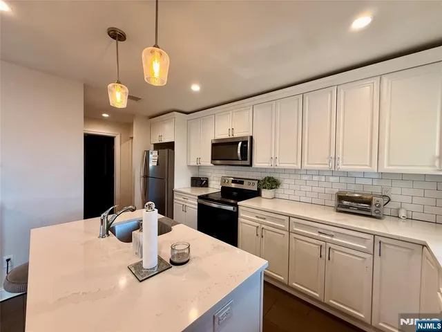 a kitchen with stainless steel appliances granite countertop a sink dishwasher a stove a refrigerator a microwave oven with white cabinets and wooden floor