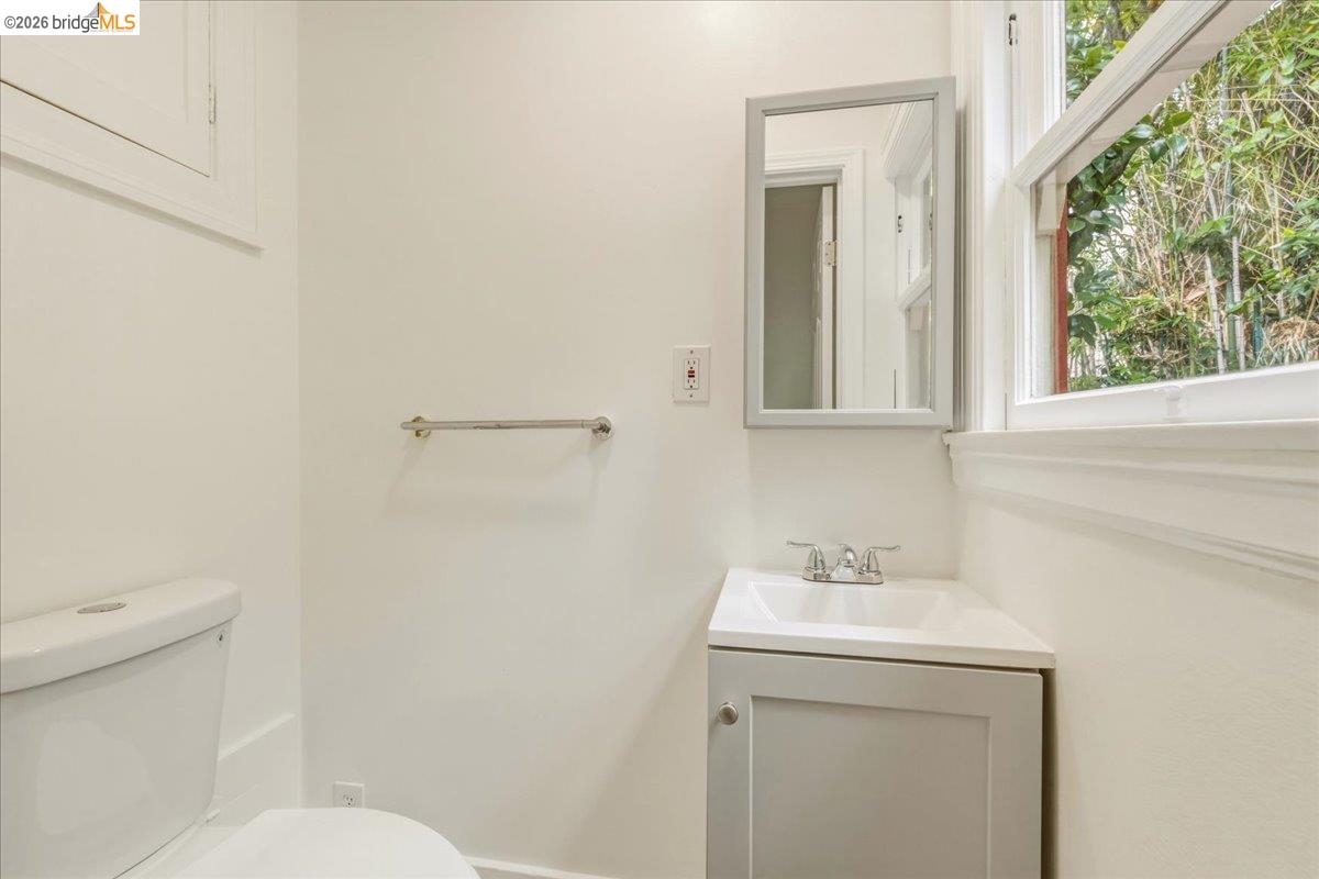 2403 Cedar Street Berkeley, CA 94708 - Photo 27 of 33 Compact bathroom featuring a white toilet, corner vanity with integrated sink, framed mirror, and a window providing natural light