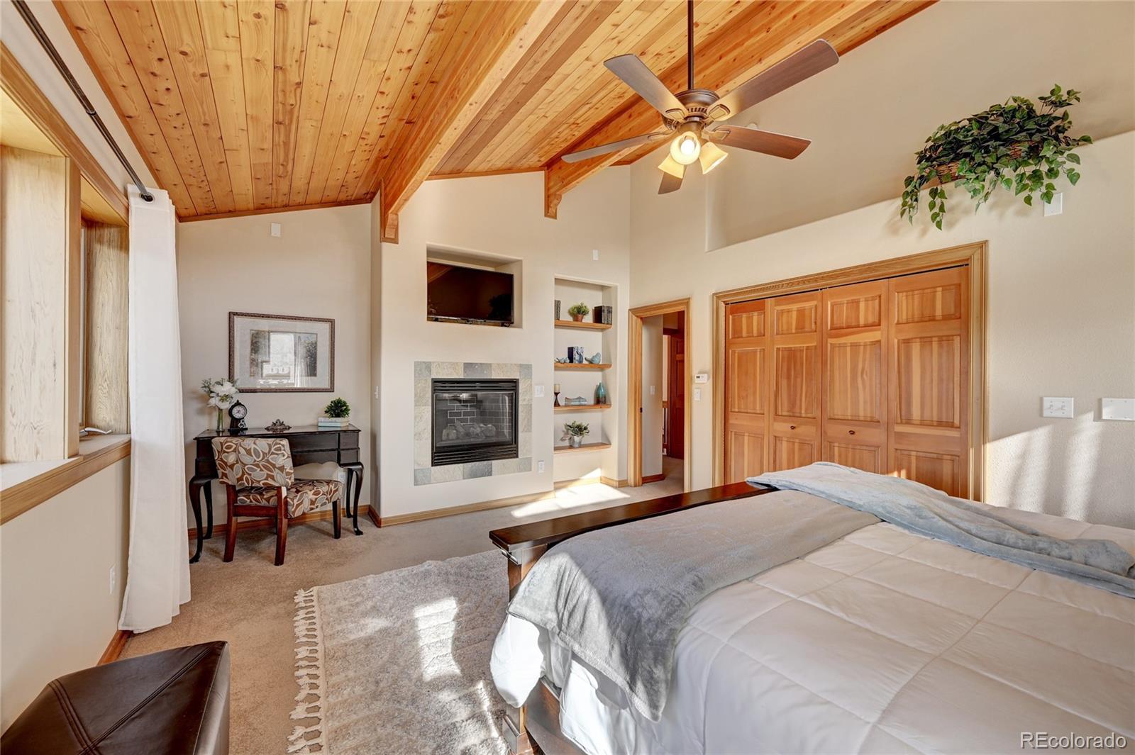 27164 Sun Ridge Drive Evergreen, CO 80439 - Photo 20 of 40 a spacious bedroom with a large bed a flat tv screen and a fireplace with wooden floor