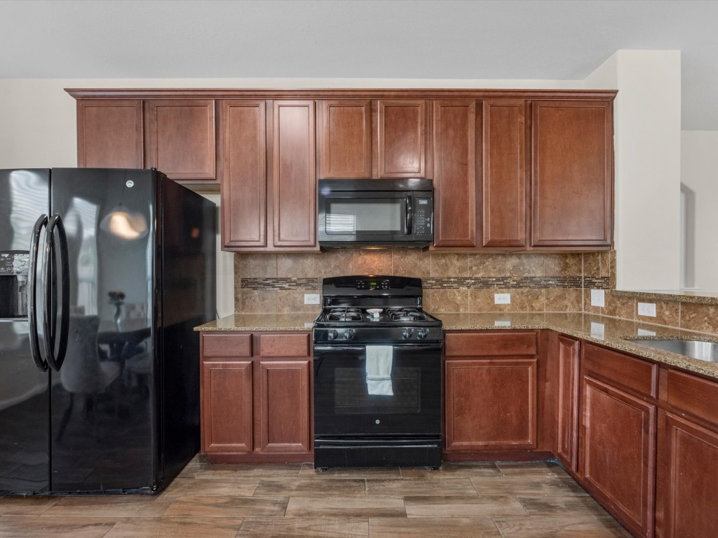 21554 Rainfall Park Drive Spring, TX 77388 - Photo 10 of 36 This kitchen features wooden cabinets, black appliance suite including a refrigerator, oven, and microwave, with a tile backsplash and granite countertops.