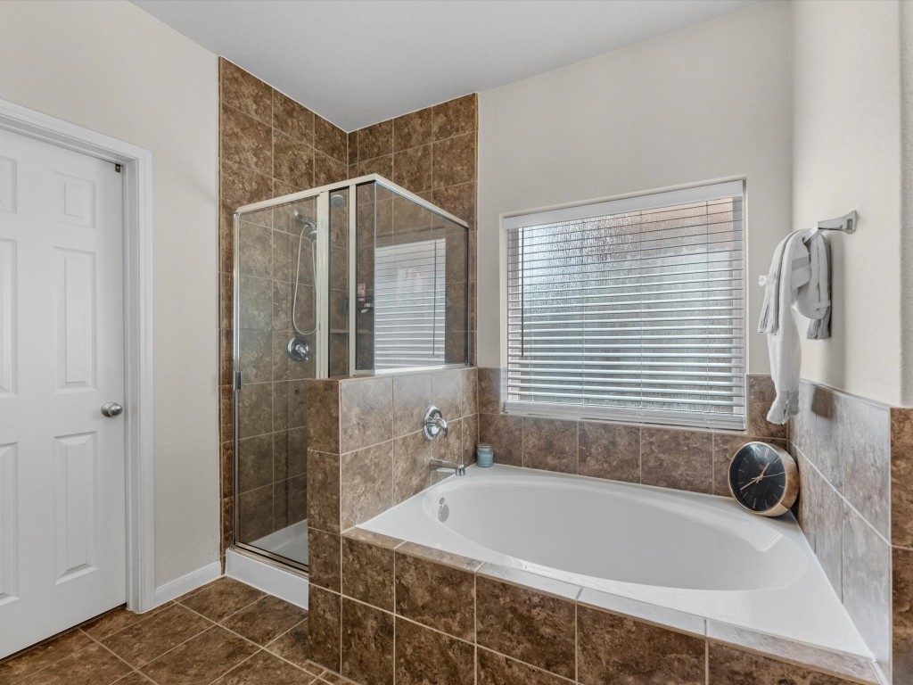 21554 Rainfall Park Drive Spring, TX 77388 - Photo 19 of 36 The primary bathroom features a spacious soaking bathtub and a separate glass-enclosed shower. A large window provides natural light, and there’s a convenient towel rack nearby.