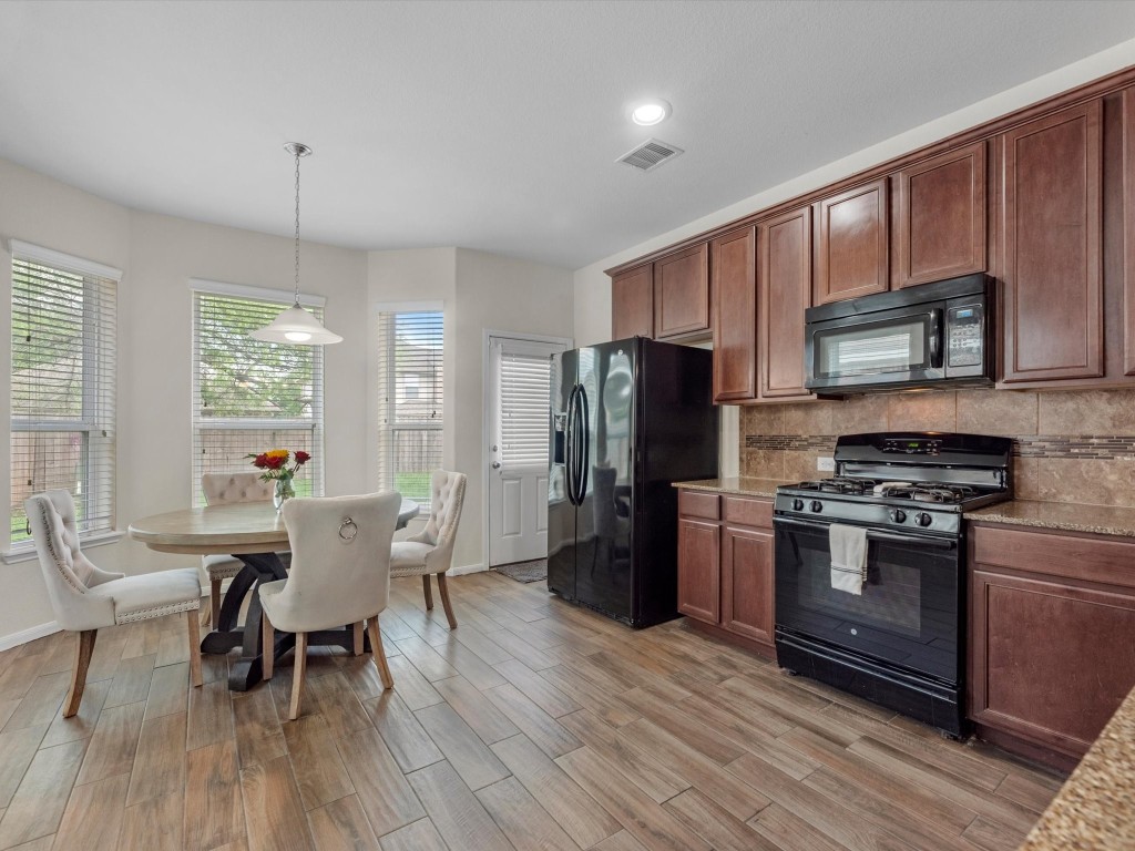 21554 Rainfall Park Drive Spring, TX 77388 - Photo 8 of 36 This kitchen features dark wood cabinetry, a sleek black appliance suite, and a cozy dining nook with ample natural light from the windows. The space is accented by wood-look tile flooring for a warm, inviting feel.