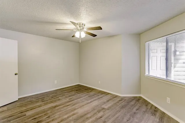 an empty room with wooden floor fan and windows