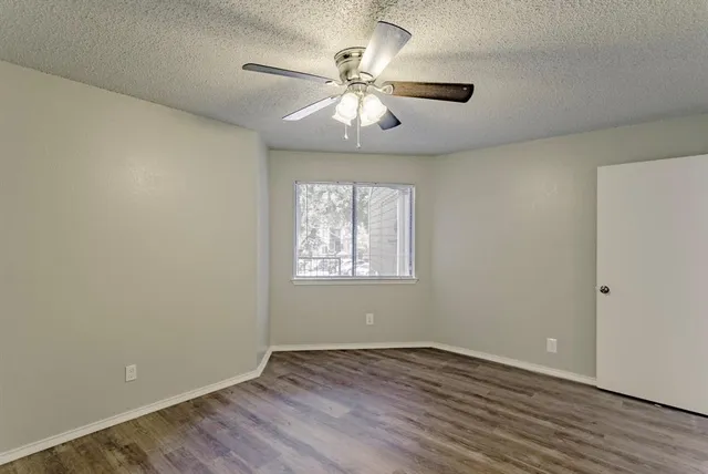 an empty room with wooden floor chandelier fan and windows