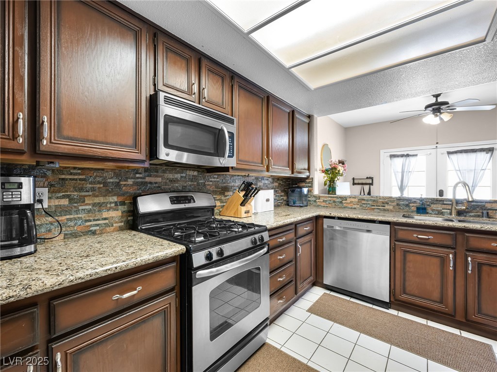 353 Seine Way, Unit N Henderson, NV 89014 - Photo 13 of 36 Kitchen featuring a ceiling fan, light tile patterned flooring, a sink, decorative backsplash, and appliances with stainless steel finishes.